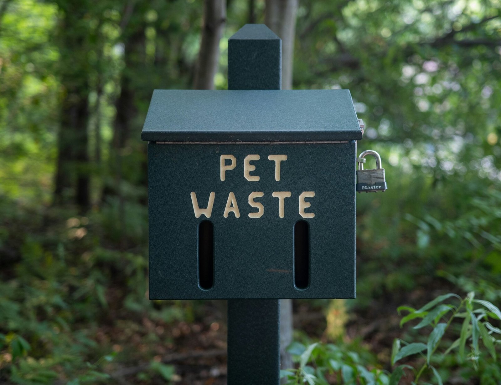 A sign that says pet waste in a wooded area